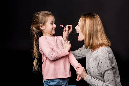兴奋的母亲试图用口红在微笑的小女儿身上涂唇膏图片