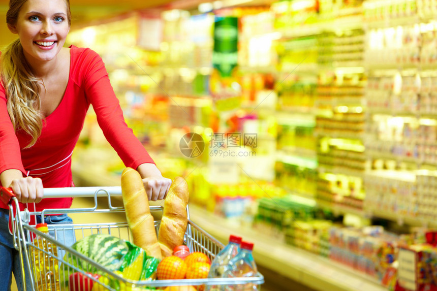 一位年轻女子在杂货店边拉着一辆装满食品的购物车图片