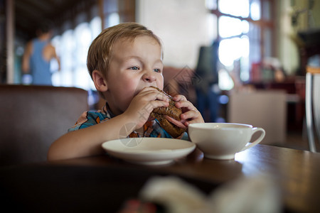 小男孩在咖啡馆吃着美味的三明治图片
