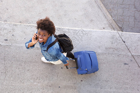 微笑的年轻女子带着行李在街上行走和用手机说图片