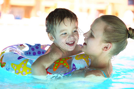 母亲和她的小儿子带着漂浮环在游泳池的粗水中游来去图片