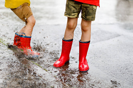 两个穿着红雨靴的小孩跳进水坑里图片