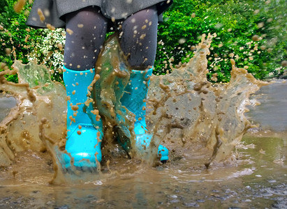 穿蓝色雨靴的孩子跳进水坑特写图片