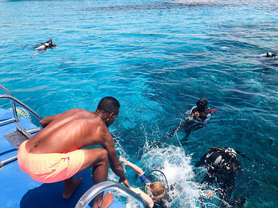 一个黑黝的阿拉伯运动健将帮助穿着黑色水肺潜水服的潜水员带着氧气瓶沉入大海中透明的蓝色海水下背景图片