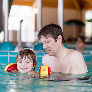 可爱的小男孩和他父亲在游泳池玩得开心快乐活跃的男孩穿着安全的游泳图片