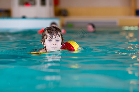 有游泳的有趣的学龄前小男孩在室内游泳池里学习游泳图片