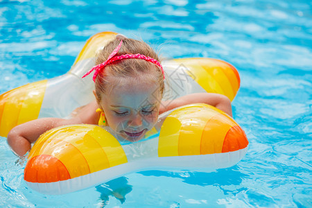 有趣的小女孩在黄色救生圈的游泳池里游泳在海图片