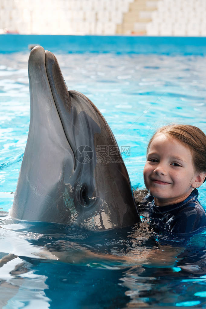 KidandDolphin女孩在蓝水中与瓶鼻海豚游泳并拥抱图片