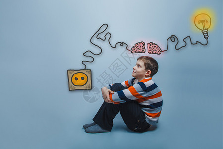 大脑助推器坐在地板上的少年男孩他的双腿抬起头来微笑着思考大脑助器充电插背景