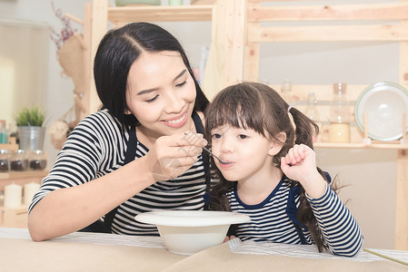 亚洲妈幸福的家庭早上给她可爱的女儿喂健康的早餐家庭孩子和快乐的人概图片