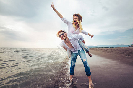 快乐的情侣在沙滩暑假上相爱快乐的女人骑着年轻图片