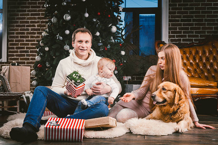 父亲妈和孩子一岁的白种女人坐在圣诞树旁边的地板上图片