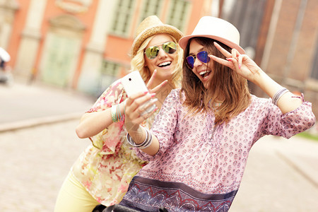 一张两个女孩朋友在骑自行车时使用智能手机的照图片
