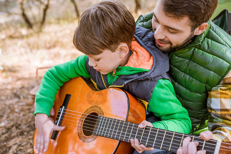 微笑的父亲在户外弹吉他时教儿子玩吉他图片