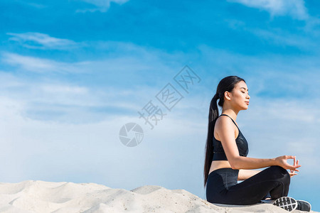 在莲花瑜伽中冥想的亚洲女与青沙泥土一起在图片