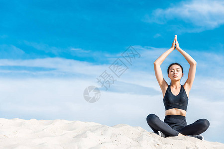 在莲花瑜伽中冥想的亚洲女和在沙面与云天图片