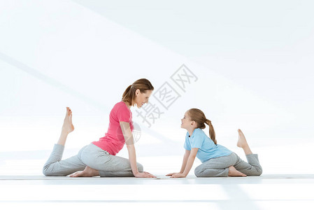 母亲和女儿微笑在垫子上做瑜伽姿势图片