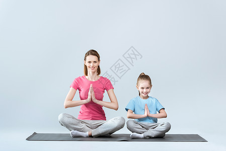 微笑运动的母亲和女儿练习莲花瑜伽姿势和在灰色上隔图片
