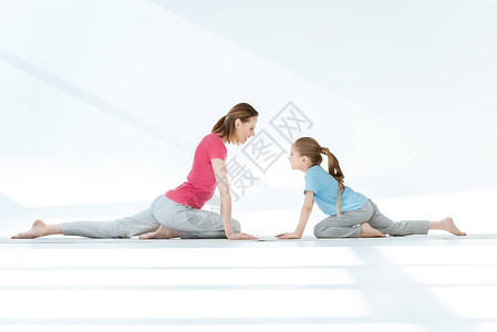 微笑的母亲和女儿在垫子上做瑜伽图片