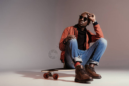 坐在长板上的时尚年轻非裔美国滑板手图片
