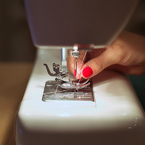 在缝纫机上缝制织物的特写女手图片