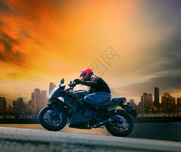 年轻的年轻人和安全西装骑着大摩托车对抗美丽的黄天空和城市景色图片