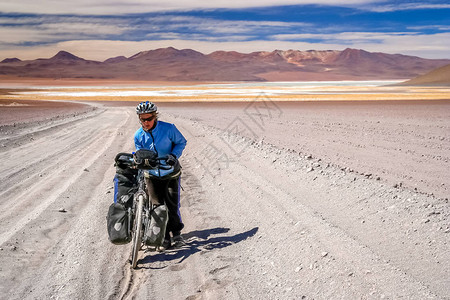 妇女骑自行车者在玻利维亚阿尔提普拉诺的沙地上挣扎并推图片