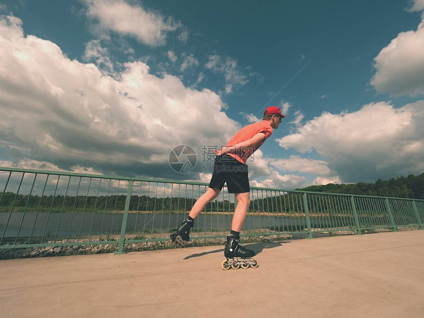 身穿t恤和黑色裤子的直排轮滑员在桥上滑冰的后视图在湖桥上光滑的混凝土地面上进行户外直排轮滑穿着四轮靴子图片