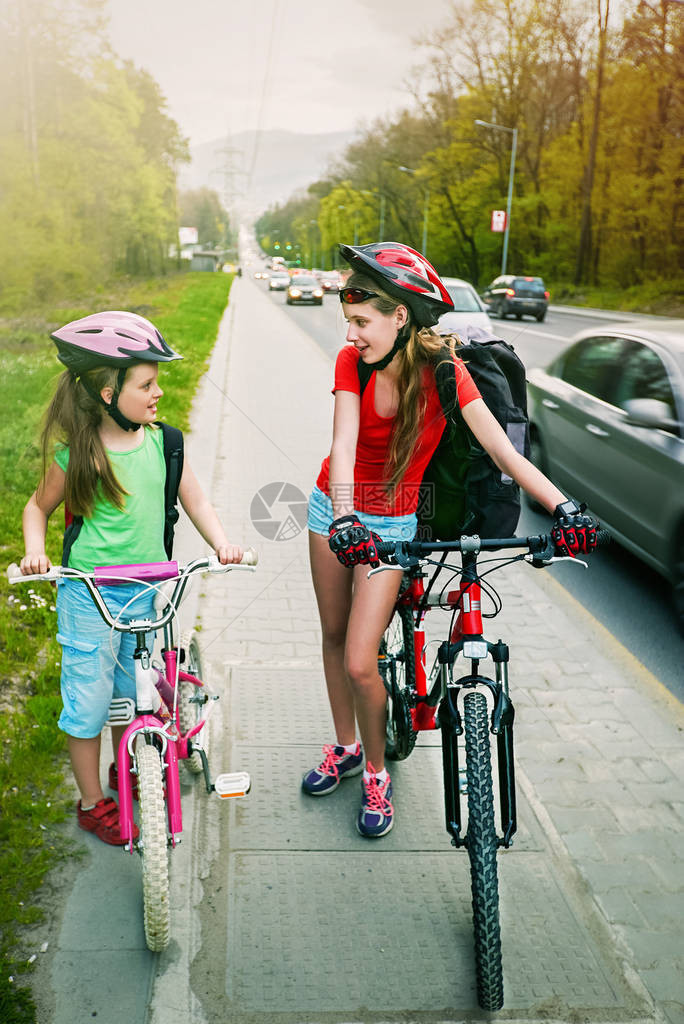 骑自行车的女孩戴着自行车头盔和玻璃背囊ciclyng孩子们在城市街道的黄色自行车道上骑自行车不期而遇的朋友聚会建议孩图片