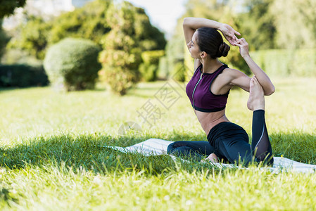 鸽子姿势的美女在户外草地上练习瑜伽图片
