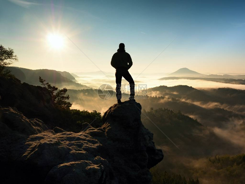山顶上的人徒步旅行者爬上了雾谷上方的岩石峰顶男人看着雾蒙的早晨山谷到明图片