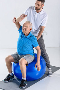 康复治疗师协助老年男子在灰色背景下参加健图片
