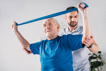 协助老年男子使用橡胶带进行锻炼的有重图片