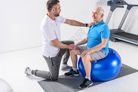 协助老年男子健身球锻炼的康复治疗图片