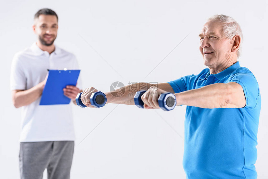 协助老年男子用在灰色上隔离的哑铃进行锻炼图片