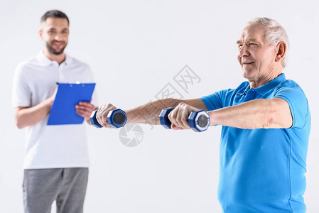 协助老年男子用在灰色上隔离的哑铃进行锻炼图片