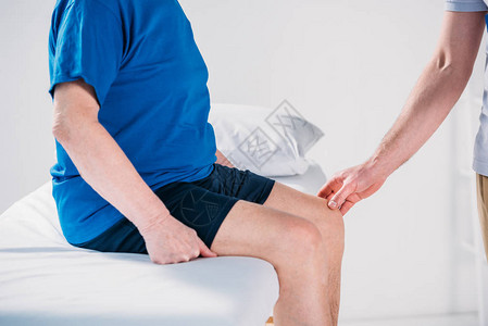 检查按摩桌上老年男子膝盖的康复治疗师图片