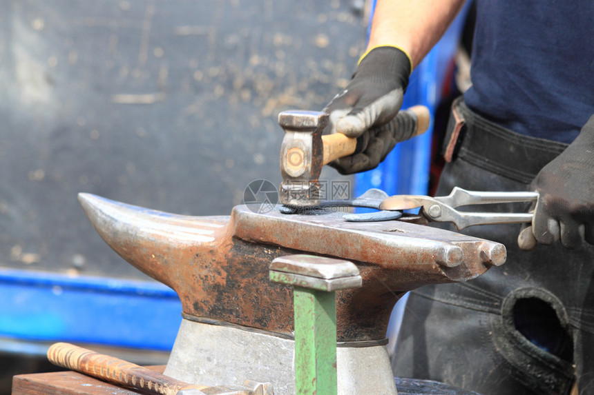 一个蹄铁匠正在用锤子敲击铁砧上的马蹄铁图片