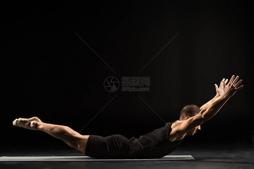 练习瑜伽的年轻运动男子在黑色隔离的瑜伽垫上做Naukas图片