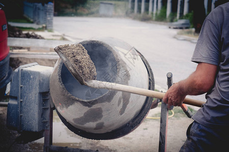 工人用铲子在混凝土搅拌机中放沙图片