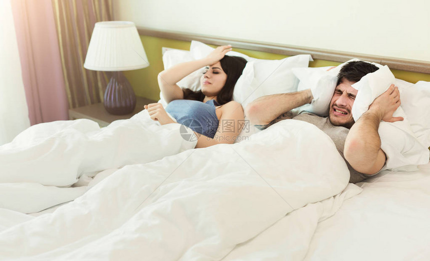 年轻不快乐的夫妇在睡觉时遮耳图片