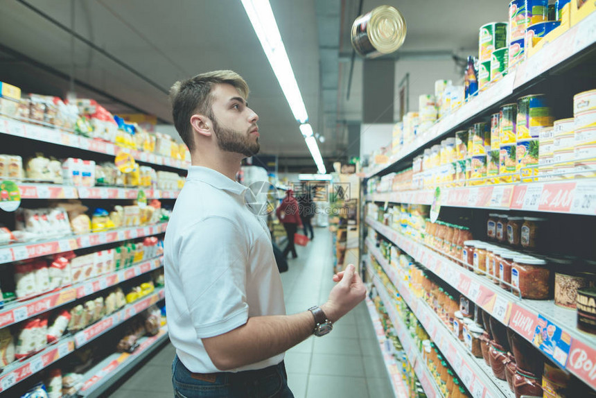 快乐的年轻人在杂货店买罐头食品一个漂亮的男人从超市货架上挑选罐头食品一个留着胡子的男人在商图片