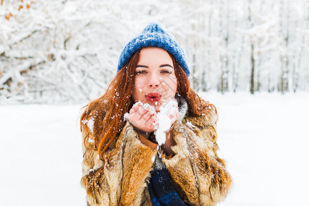 穿着蓝色编织帽子的迷人年轻女子在雪上吹风图片
