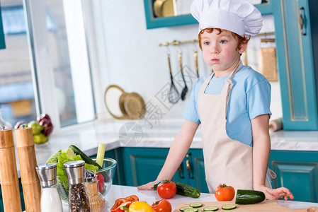穿着厨帽和围裙的可爱小可爱男孩在厨房图片