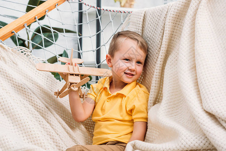 微笑的男孩在吊床上玩木制飞机玩具图片