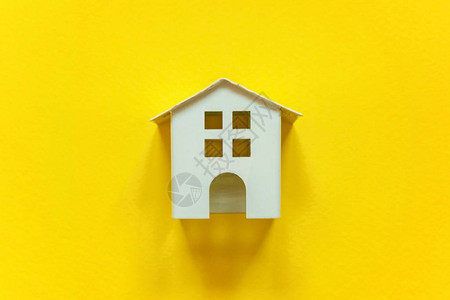 简单的平躺设计与黄色彩纸时尚背景上的微型白色玩具屋抵押财产保险图片