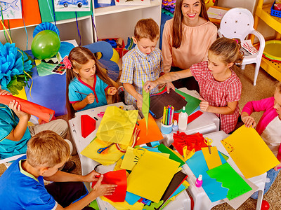 在幼稚园的桌上持有彩色纸和胶水的群组儿童群图片