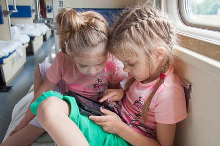 两个女孩坐在二等车厢的床上玩着电子平板图片