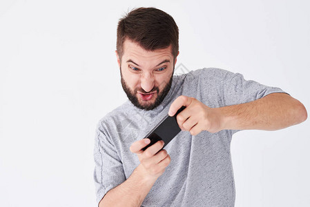 情绪化的年轻胡子男在smatphone上玩游戏的特写镜头穿着休闲服图片
