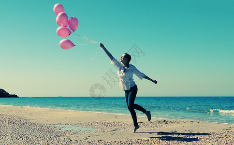 年轻女子带着粉色气球在海滩上行走图片